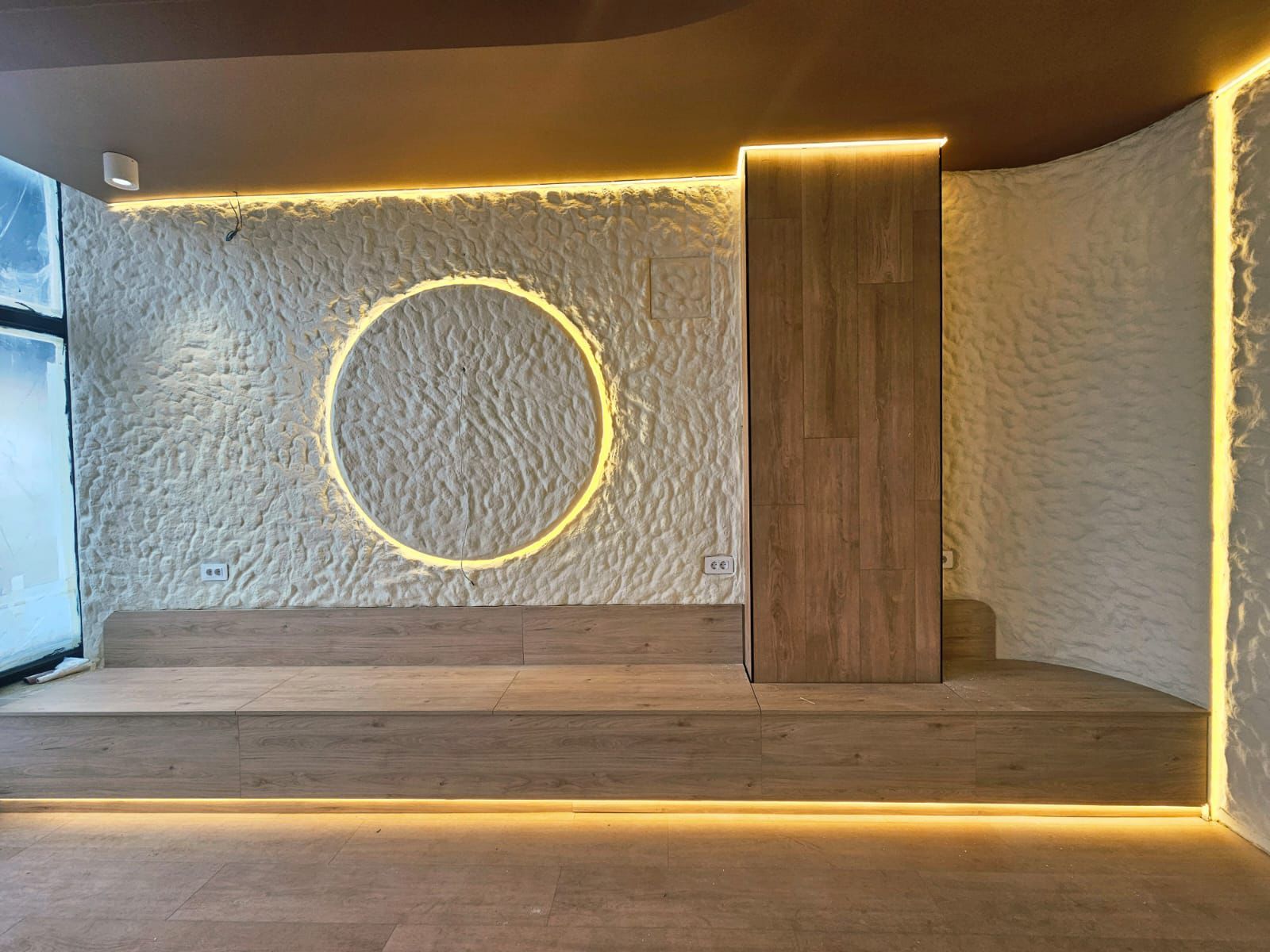 Perete cu tencuială decorativă texturată și inel luminos LED, lângă placare din lemn